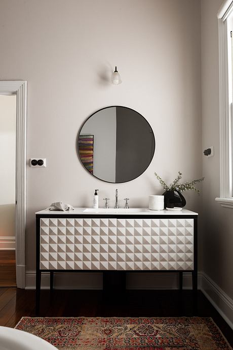 Sleek vanity with textured drawers, round mirror, and ornate rug contrast.