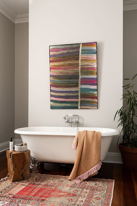 A cozy, earthy-toned bathroom with an ornate rug, freestanding tub, and textured wall art.