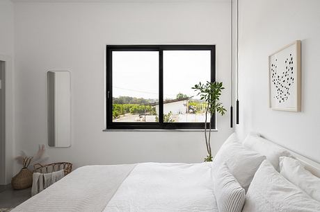 Minimalist bedroom with large windows, black frames, and a plant adding natural touch.
