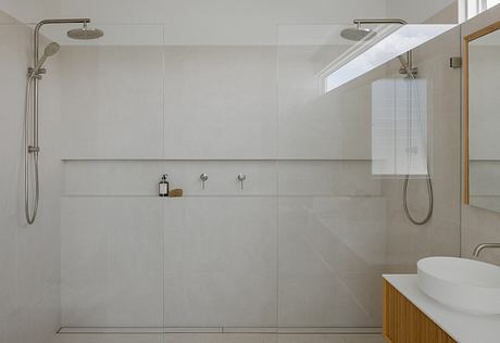 Spacious, minimalist bathroom with large, tiled shower area, modern fixtures, and natural lighting.