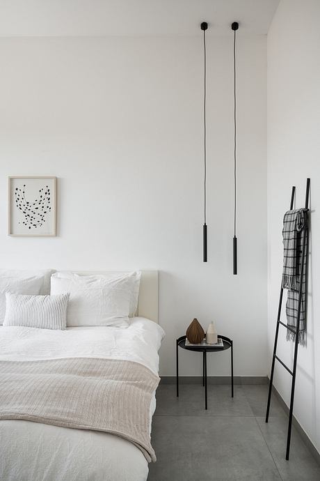 Minimalist bedroom with white walls, suspended black lamps, and a monochrome color scheme.