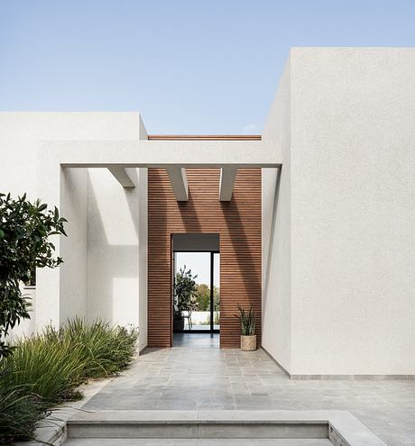 Minimalist white exterior with wooden accents, glass entryway, and lush vegetation.