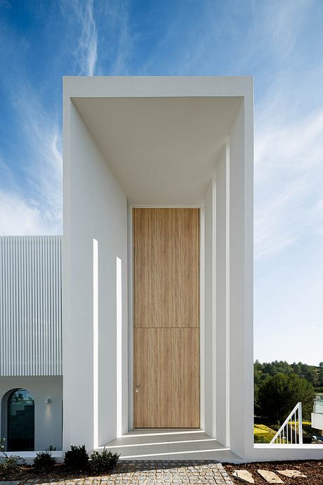 Minimalist white exterior with modern wooden door and landscaped surroundings.