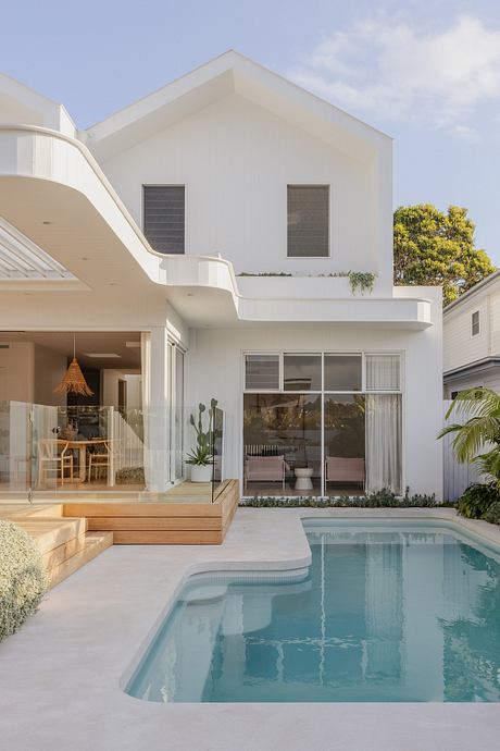 Contemporary tropical-style home with sleek white exterior, pool, and lush landscaping.