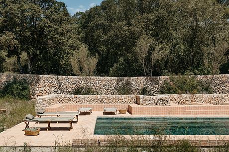 Rustic stone wall surrounding a tiled pool area with wooden benches and planters.