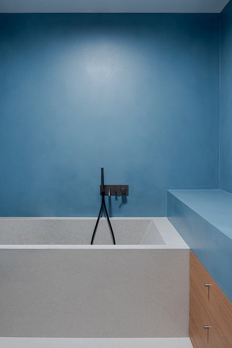Minimalist bathroom design with monotone blue walls, grey countertop, and black fixtures.