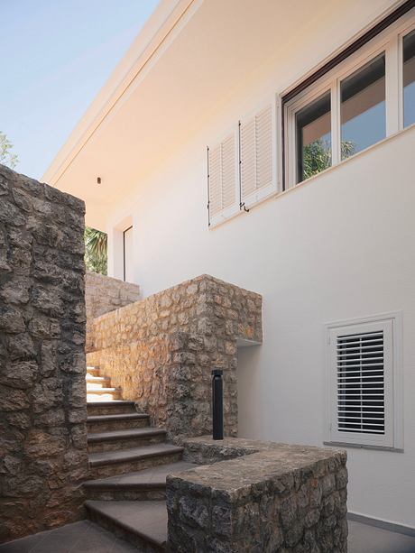 Exterior view of a modern Mediterranean-style home with stone walls and stairs.