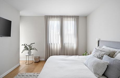A serene and cozy bedroom with minimalist decor, wooden floors, and large windows.