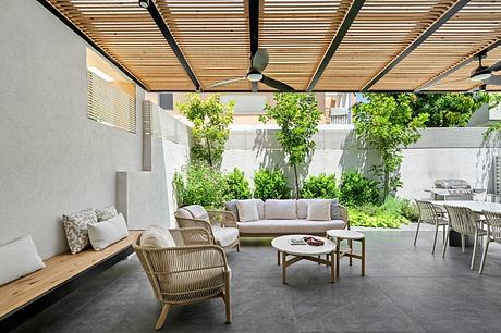 A modern outdoor living space with a slatted wooden canopy, comfortable seating, and lush greenery.