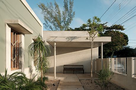 A modern concrete structure with a covered patio, lush greenery, and a bench.