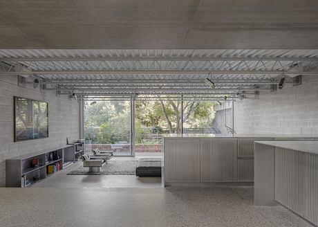 Expansive space with concrete walls, exposed ceiling trusses, and large windows overlooking nature.
