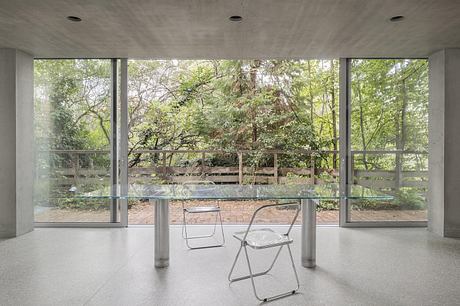 A modern, minimalist interior with a glass wall overlooking a lush, forested landscape.