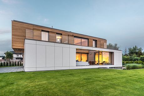 Modern two-story home with glass walls, wooden siding, and landscaped yard.