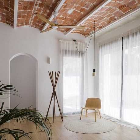 Rustic brick ceiling, minimalist wood furniture, and floor-to-ceiling windows in a cozy interior.