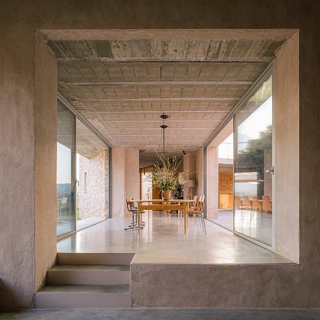 Rustic wooden ceiling with concrete floors and steps leading to a modern dining area.