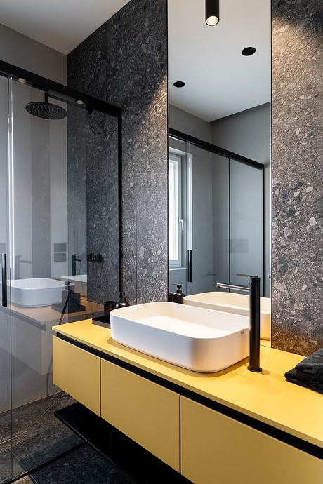 Sleek, modern bathroom with striking contrast of dark stone walls, yellow vanity, and vessel sinks.