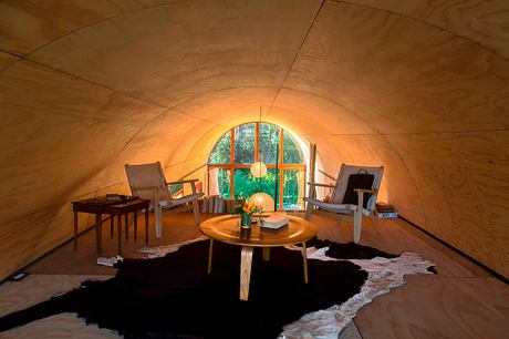 Cozy dome-shaped interior with arched windows, wooden furniture, and a plush area rug.