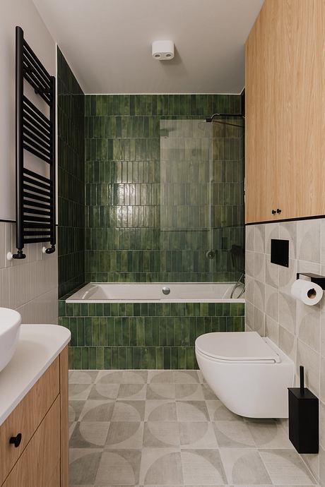 A modern bathroom with green ceramic tiles, a bathtub, and a toilet. The floor features a patterned tile design.
