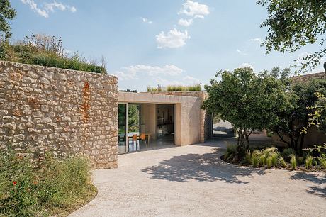 A modern, open-plan structure with a stone exterior and large glass doors, surrounded by lush greenery.