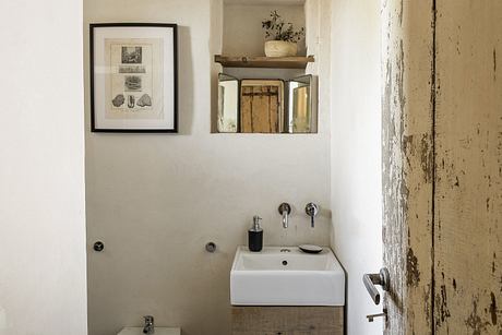 A rustic and minimalist bathroom with a vintage wooden shelf, vessel sink, and framed decor.