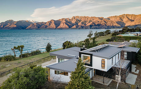 Stunning modern residential architecture overlooking a serene lake and majestic mountains.