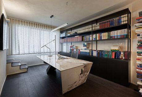 Sleek, minimalist home office with a marble-topped desk, extensive bookshelves, and modern lighting.