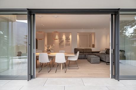 Modern open-concept living space with glass walls, neutral furnishings, and pendant lights.