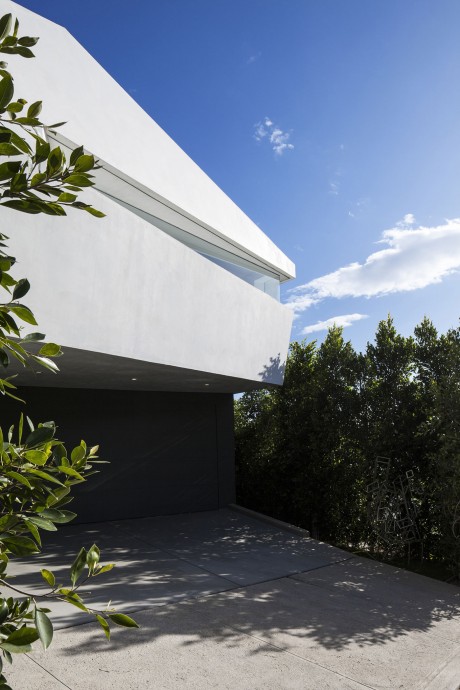 A modern, minimalist building with a sleek white exterior, cantilevered roof, and lush greenery.