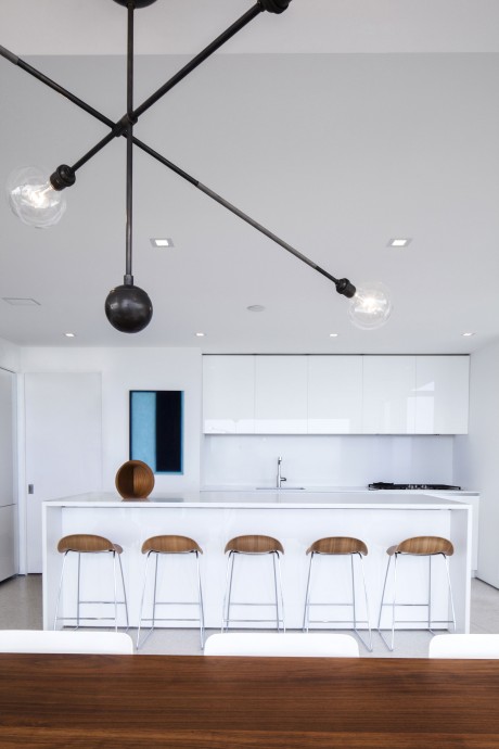 Sleek modern kitchen with minimalist white cabinetry, wooden barstools, and a black geometric pendant light fixture.