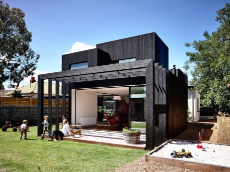 A modern, black-clad home with a large covered patio, wooden accents, and lush greenery.