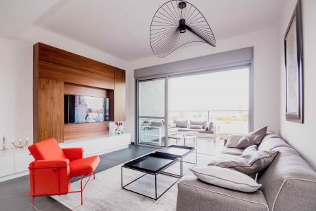 Modern living room with wooden TV unit, red armchair, and sleek furniture.