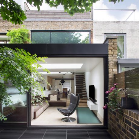 Modern glass-walled home with an open floor plan, sleek furnishings, and lush greenery.