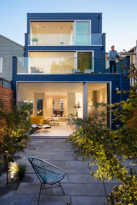 Sleek blue modern townhouse with floor-to-ceiling windows and inviting patio.