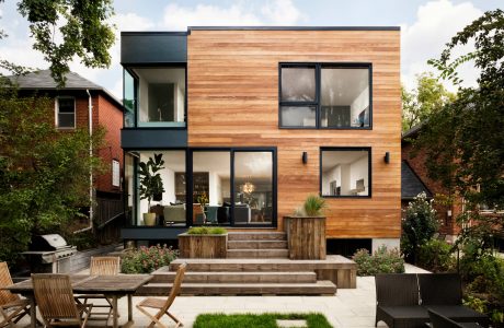 Modern two-story home with wooden siding, large windows, and an inviting outdoor patio area.