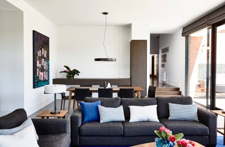 Modern open-concept living space with dark gray sofa, wood dining table, and colorful abstract artwork.