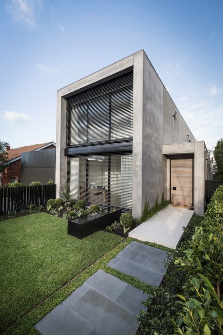 Striking modern home with sleek concrete facade, slatted blinds, and lush landscaping.