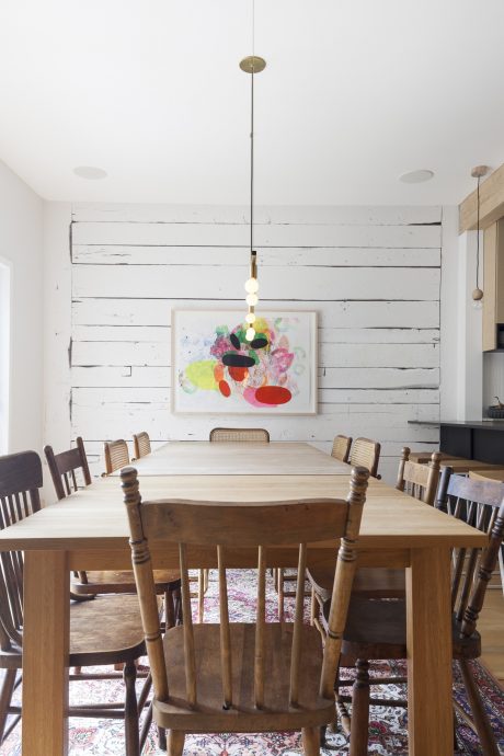 Rustic dining room with wood-paneled walls, colorful abstract artwork, and a wooden table and chairs.