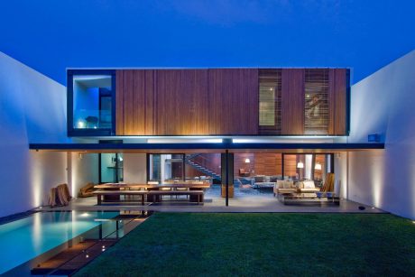 A modern, two-story home with a wooden exterior, glass walls, and an outdoor pool surrounded by greenery.