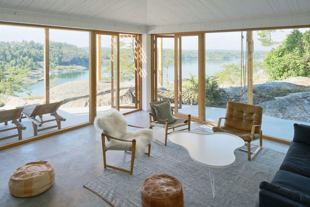 Sunlit room with modern furniture and large windows overlooking a lake.