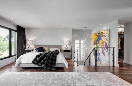 Spacious modern bedroom with hardwood floors, gray upholstered bed, and vibrant abstract art.