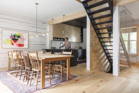 A rustic and modern open-plan kitchen with wood beams, a metal staircase, and an artistic painting.