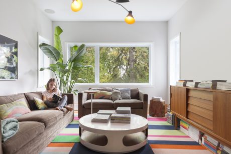 Warm, modern living room with large windows, tropical plants, and vibrant patterned rug.