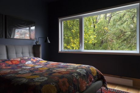 Cozy bedroom with vibrant floral bedding, dark walls, and large window overlooking lush greenery.