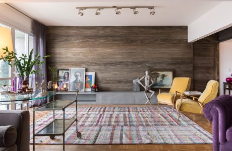 This eclectic living room features a rustic wood accent wall, colorful area rug, and mix of furniture styles.