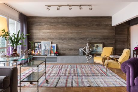 This eclectic living room features a rustic wood accent wall, colorful area rug, and mix of furniture styles.