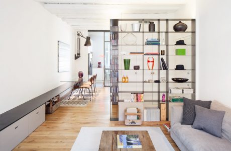 Modern open-concept living space with shelving unit, wooden floors, and natural lighting.