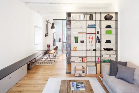 Modern open-concept living space with shelving unit, wooden floors, and natural lighting.