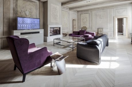 Ornate, high-ceilinged room with plush purple furniture, glass coffee table, and intricate wall carvings.