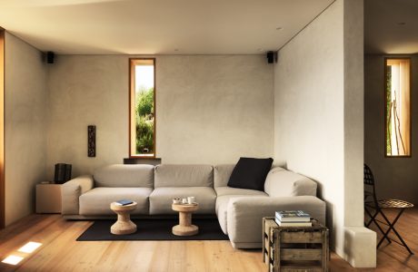 Minimalist living room with wooden floors, neutral-toned sofa, and natural light from windows.
