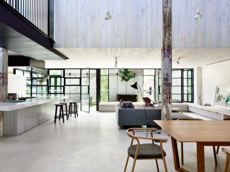 An open-concept interior with a rustic wooden ceiling, modern furnishings, and a tree-filled view.